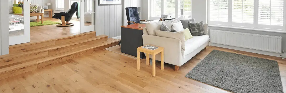 A modern living room with professionally installed laminate flooring, a beige sofa, a small side table, a gray rug, and large windows with white shutters in Syracuse, NY